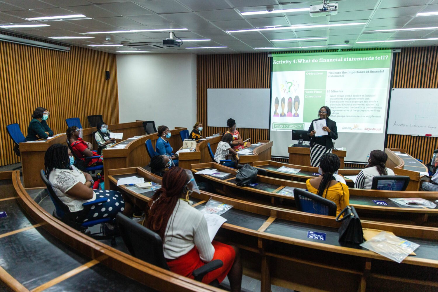 A classroom of women diligently learning. A Road to Growth trainer stands at the front before a screen.