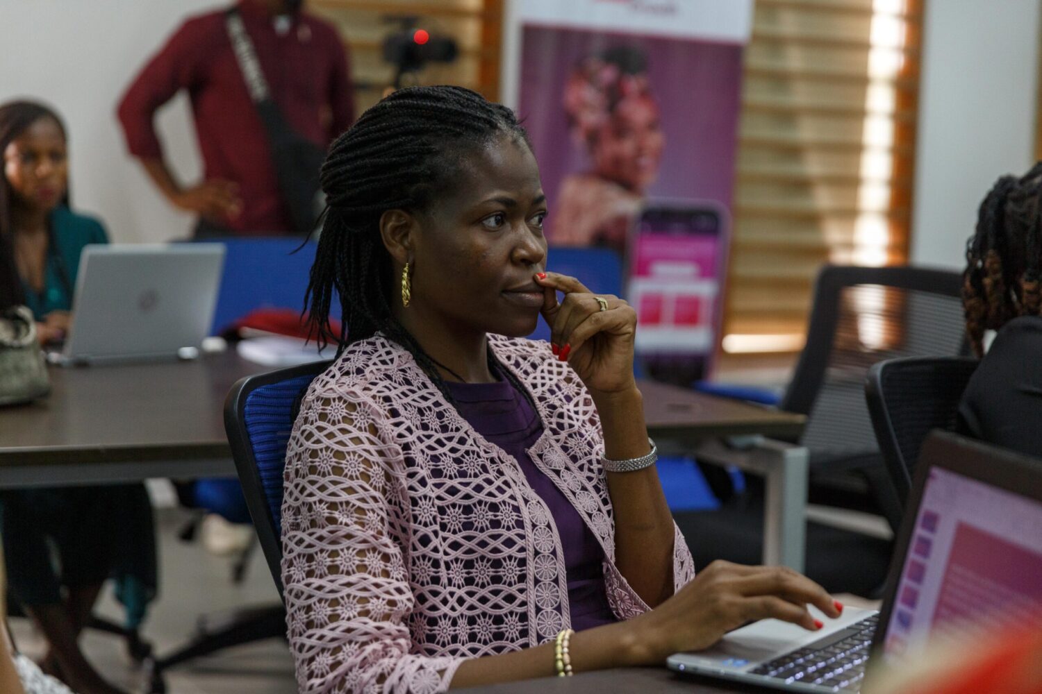 A woman in a purple cardigan is learning on a laptop with a look of concentration on her face