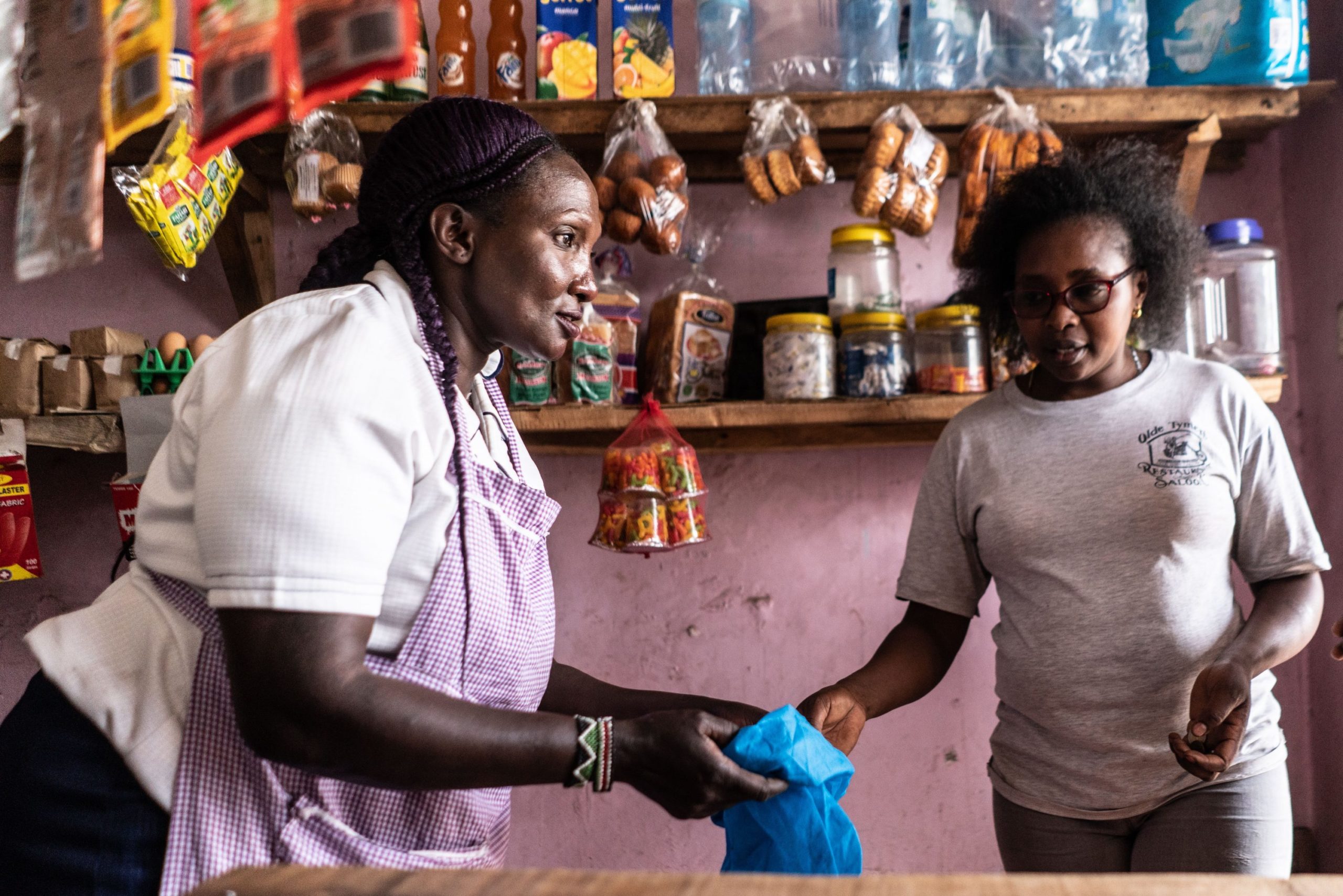 Asilia Nduku, HerVenture user in Kenya serves a customer at her grocery shop.