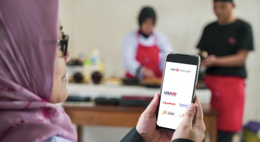 Woman entrepreneur holds up the HerVenture app at her business