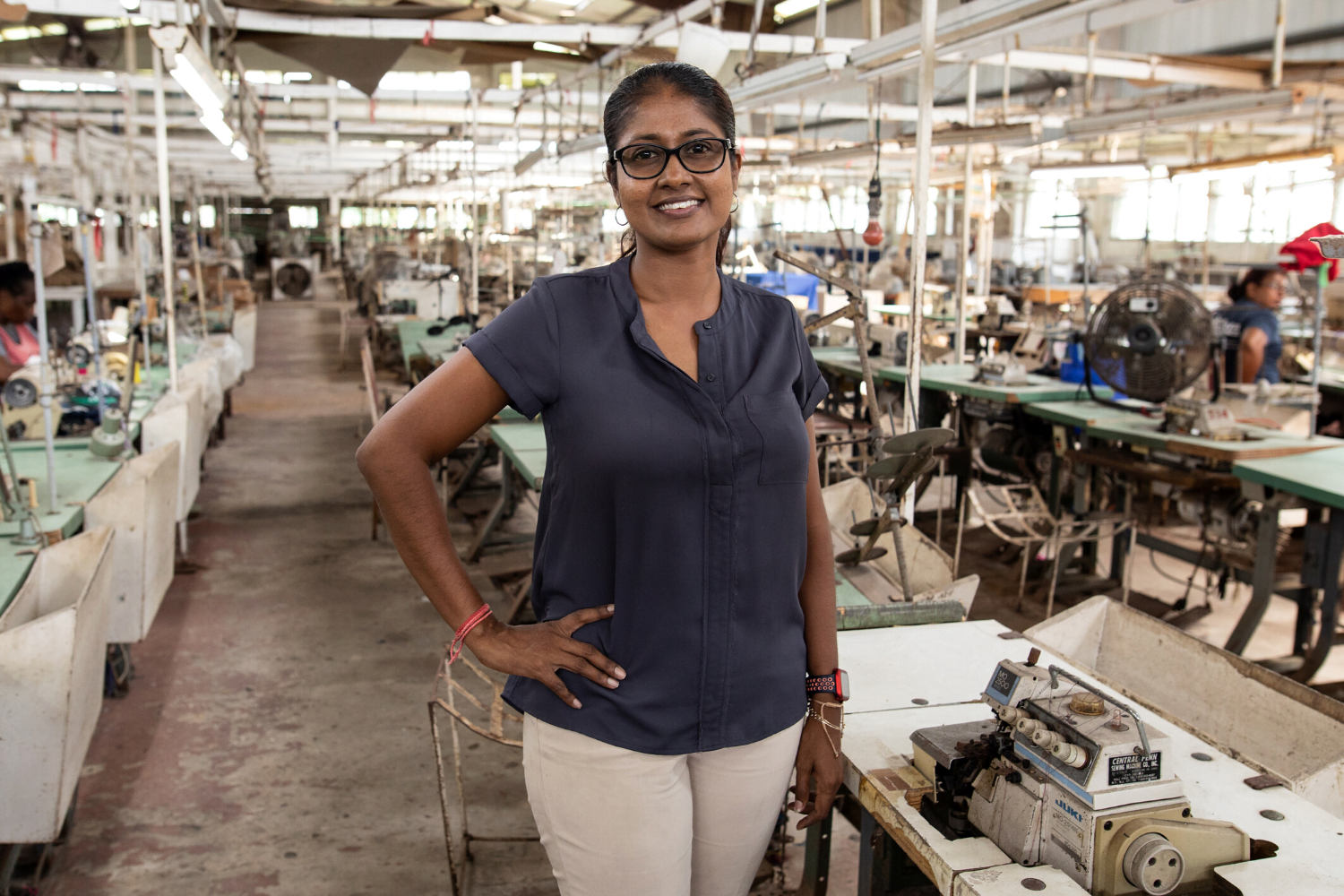 Upasna Mudlier poses in front of sewing machines at Denmor Garments