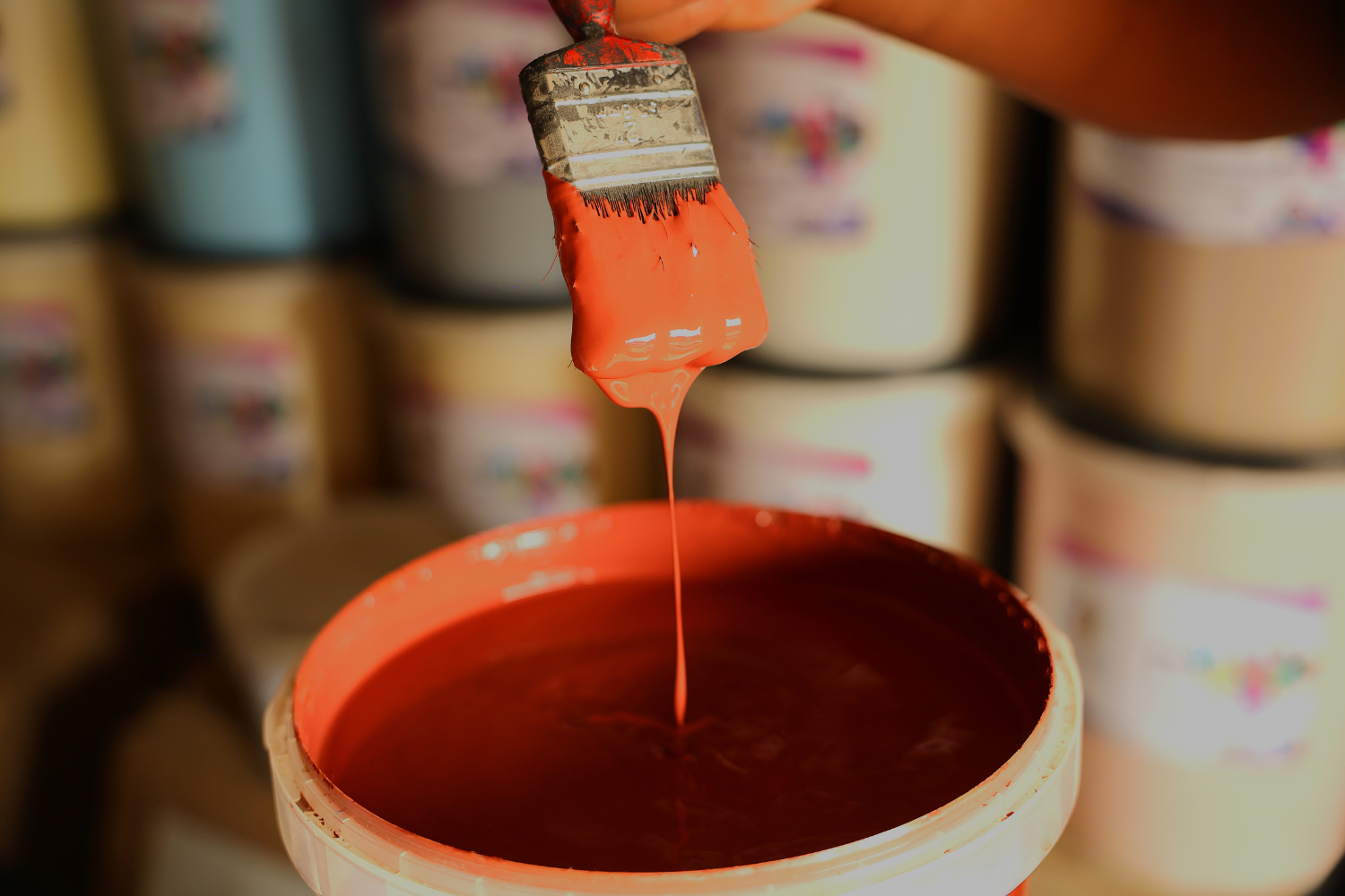 A paintbrush dripping red paint into a tub full of the same red paint.