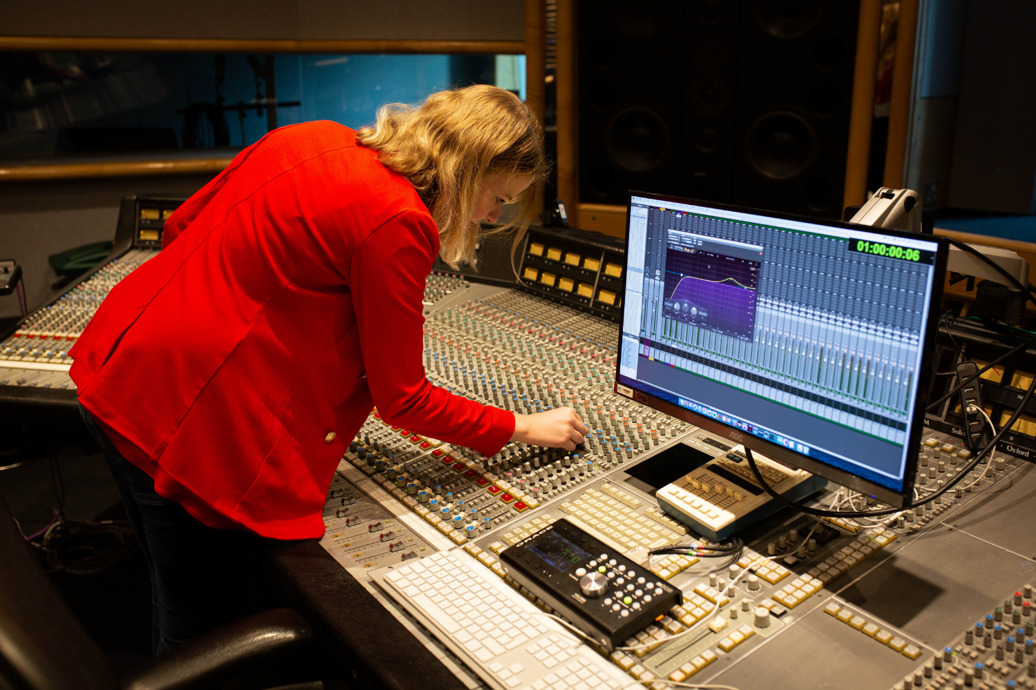 Olga FitzRoy, a British self-employed sound engineer, sits at a sound desk with hundreds of buttons on it. Her right hand is tweaking one of the buttons.