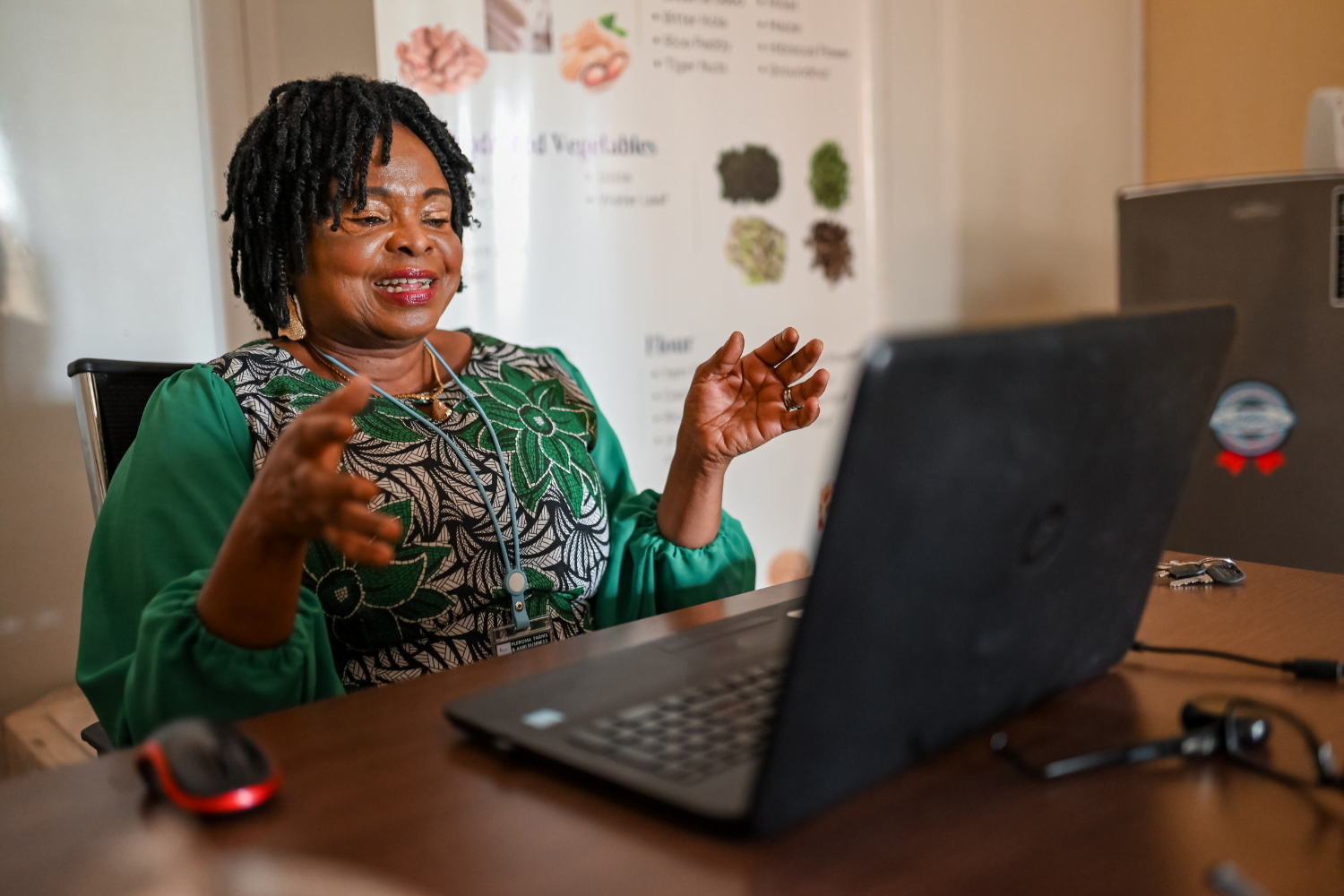 Ellah Omezi, a Nigerian woman entrepreneur wearing a green embroidered dress, talks animatedly in front of her laptop. It looks like she is on a video call.