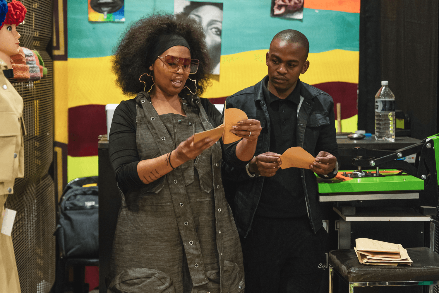 Nkeletseng Tsetsane, a woman entrepreneur in South Africa, is showing the man next to her what to do with some circular pieces of brown paper. Both have the paper in their hands and are looking at Nkeletseng's hands as she explains.
