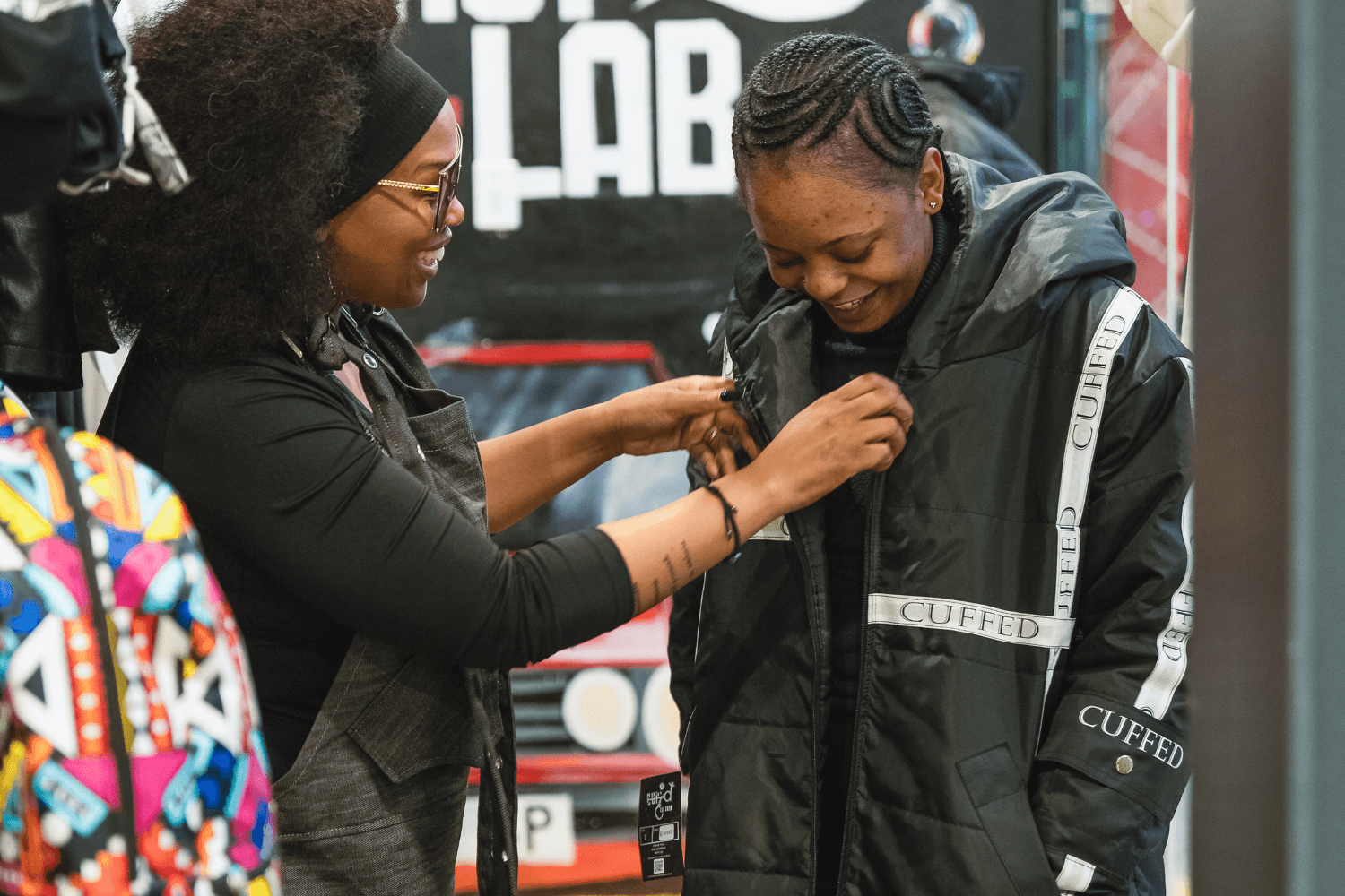Nkeletseng Tsetsane, a woman entrepreneur in South Africa, adjusts a black coat on the customer in front of her. She is smiling and talking to the customer, who looks down at the coat.