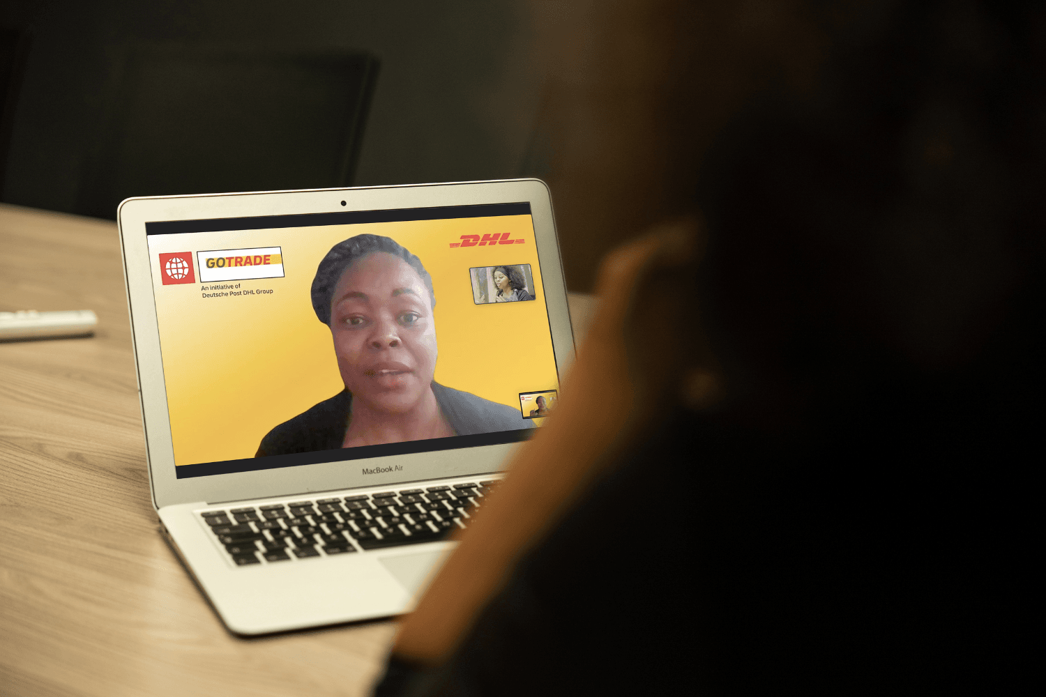 A laptop on the wooden table. The laptop shows mentor, Glory Mutai from Kenya. The camera is looking over the shoulder of someone who Glory is talking to.