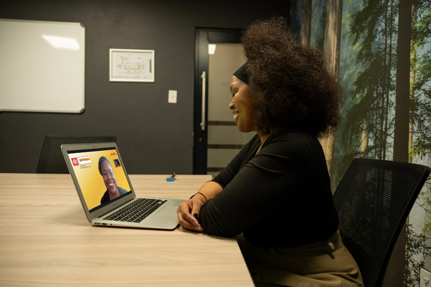 Nkeletseng Tsetsane, a woman entrepreneur in South Africa, smiles as she leans her arms against a wooden table. In front of her on the wooden table is a laptop with a woman on the screen. This is her mentor, Glory Mutai from Kenya. The two of them are smiling at each other.