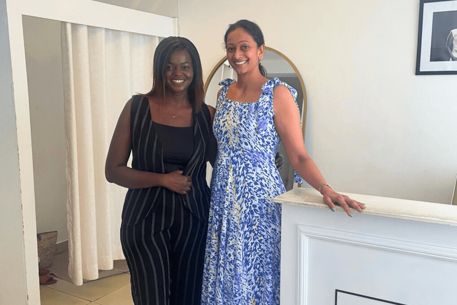 Kenyan woman entrepreneur, Joy Obuya poses for a photo with Dhivya O'Connor, CEO of the Cherie Blair Foundation for Women. They are inside Joy's shop, where she sells sustainably made clothing. Dhivya is wearing a blue and white sun dress from the brand.