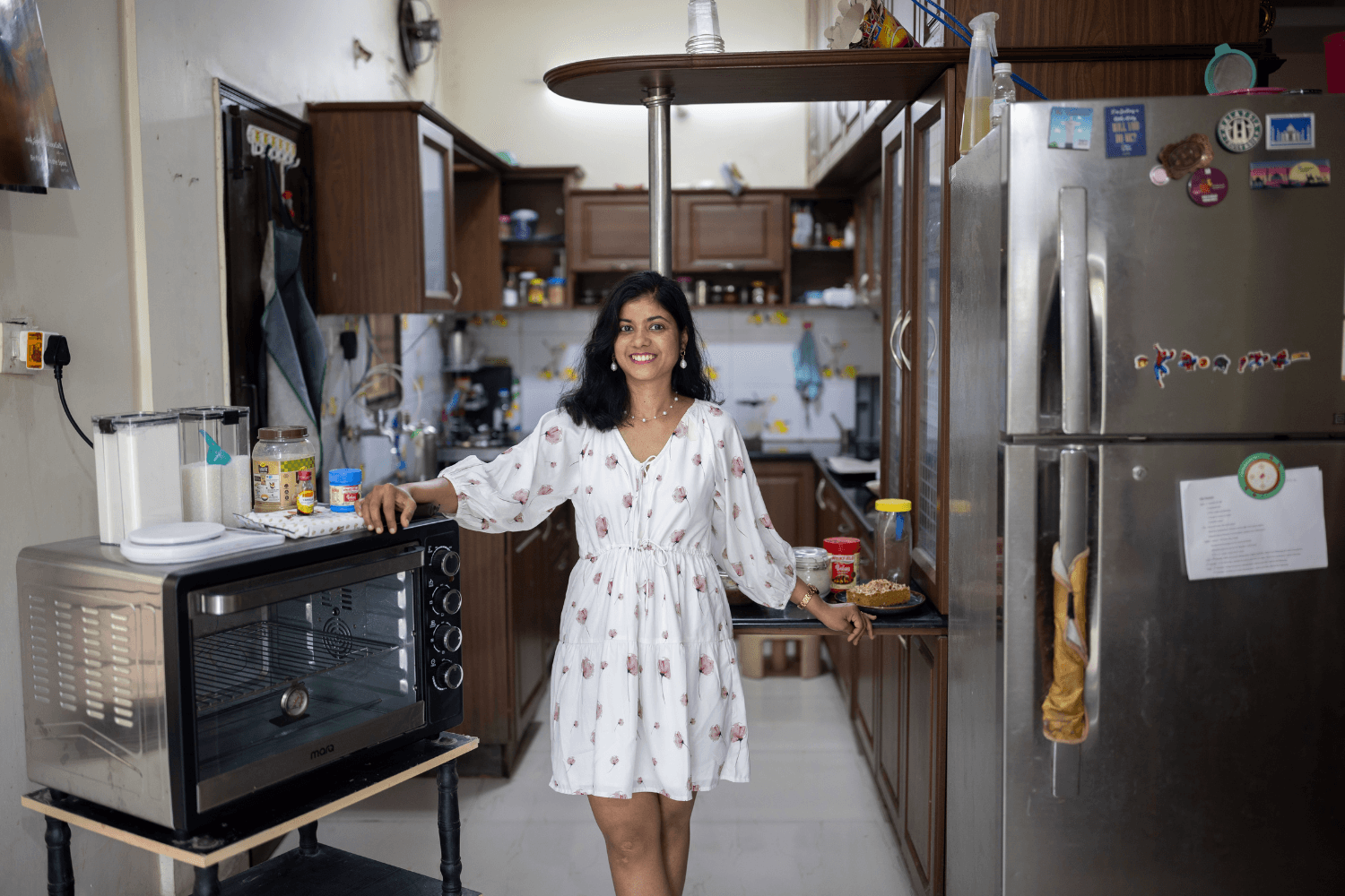 Prachi Robinson, a woman entrepreneur from India stands in the middle of a kitchen. She is smiling at the camera, with one hand resting on an oven and the other on a countertop.
