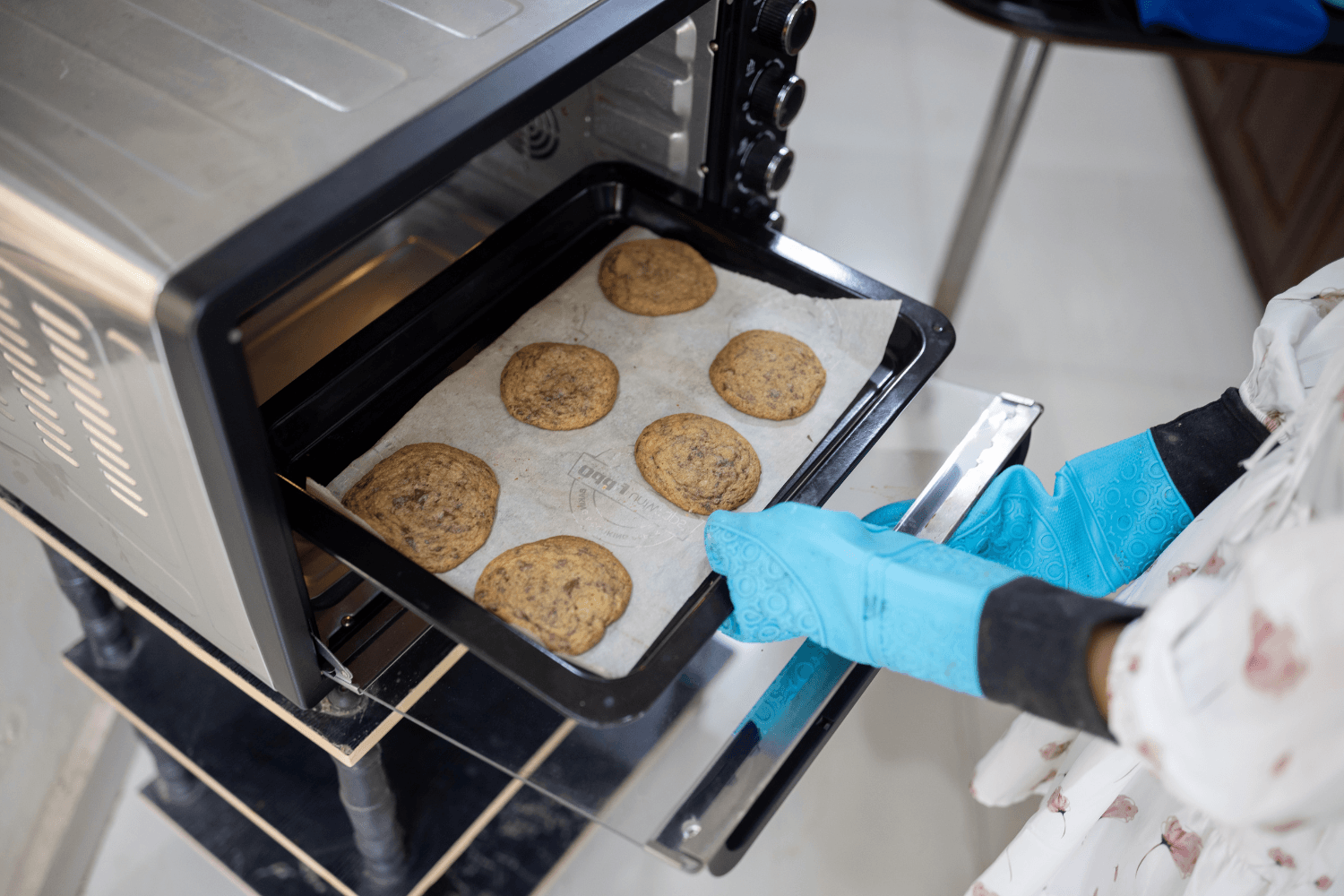 Cookies are taken out of the oven by hands wearing oven gloves.