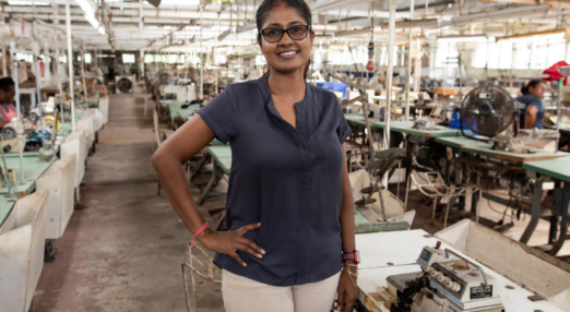 Upasna Mudlier poses in front of sewing machines at Denmor Garments