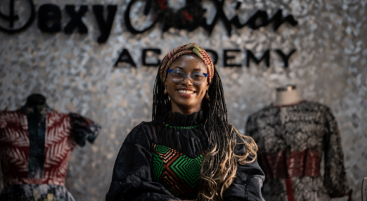 Adaeze Onu, Creative Director of Dexycreation in Nigeria, smiles in front of two dresses she designed.